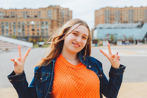 Uma adolescente mostra um sinal legal em forma de v enquanto caminha na cidade Adolescente feliz, emoções positivas e sorridentes de uma geração adolescente z