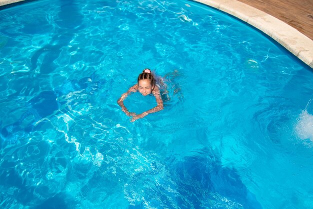 Uma adolescente nada em uma piscina com água azul. Ela tem tranças africanas trançadas com fitas zi-zi.