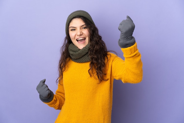 Uma adolescente russa com chapéu de inverno isolada em um fundo roxo comemorando uma vitória