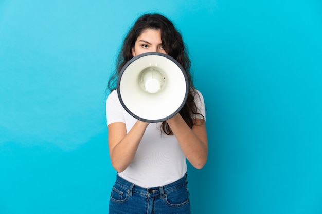 Foto uma adolescente russa isolada em um fundo azul gritando em um megafone para anunciar algo