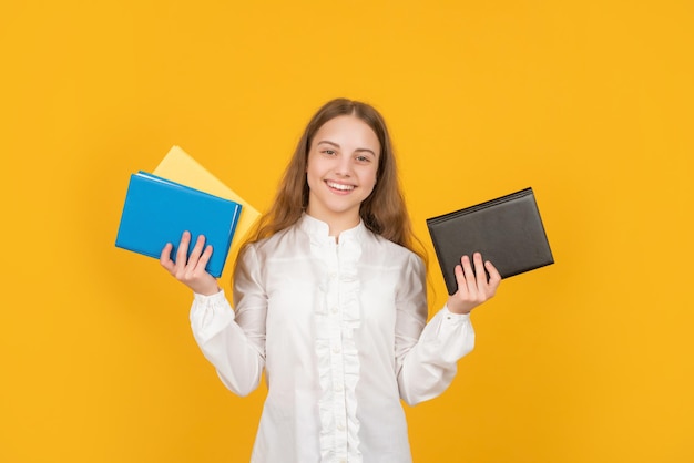 Uma adolescente sorridente segura o livro de exercícios da escola sobre o estudo de fundo amarelo