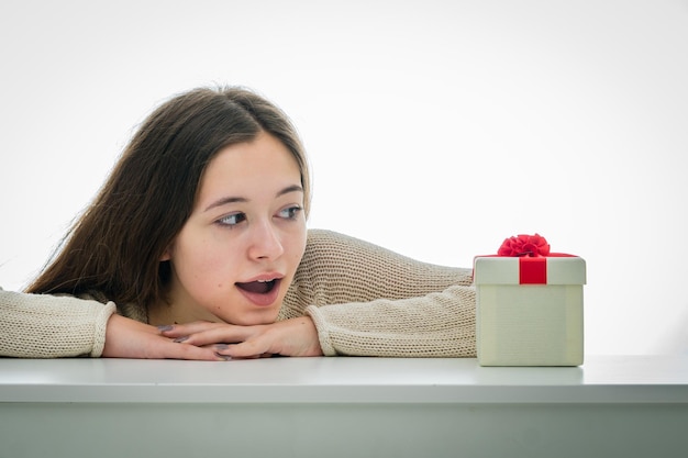 Uma adolescente surpresa está olhando para uma caixa de presentes contra um fundo branco