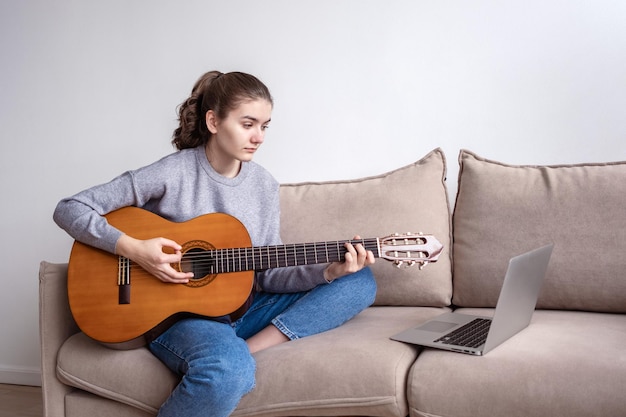 Foto uma adolescente tocando violão durante elearning na frente de um laptop em casa no sofá