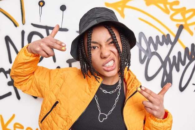 Foto uma adolescente urbana descolada com dreadlocks faz gestos de yo contra obras de arte de grafite vestidas com roupas da moda ou roupas da moda de rua parece legal