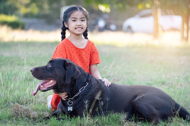 Uma adorável menina criança do sudeste asiático em trajes vermelhos brinca com seu cachorro grande no quintal ou no quintal da frente à noite. Conceito de amante de animais de estimação