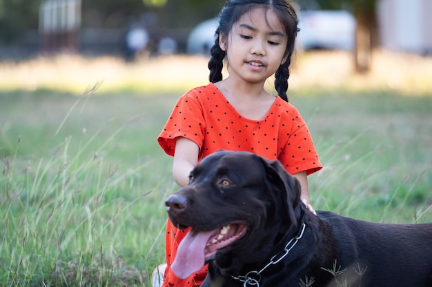 Uma adorável menina criança do sudeste asiático em trajes vermelhos brinca com seu cachorro grande no quintal ou no quintal da frente à noite. Conceito de amante de animais de estimação