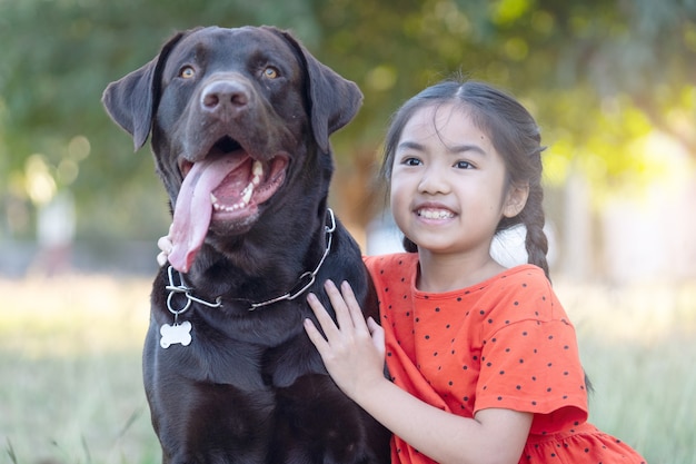Uma adorável menina criança do sudeste asiático em trajes vermelhos brinca com seu cachorro grande no quintal ou no quintal da frente à noite. Conceito de amante de animais de estimação