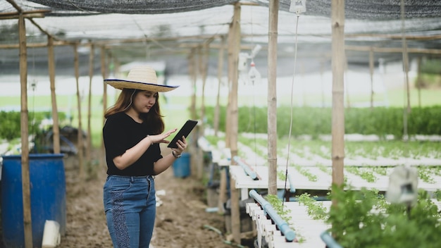 Uma agricultora adolescente usa um aplicativo de tablet para controlar o cultivo de vegetais em estufa, fazenda inteligente.