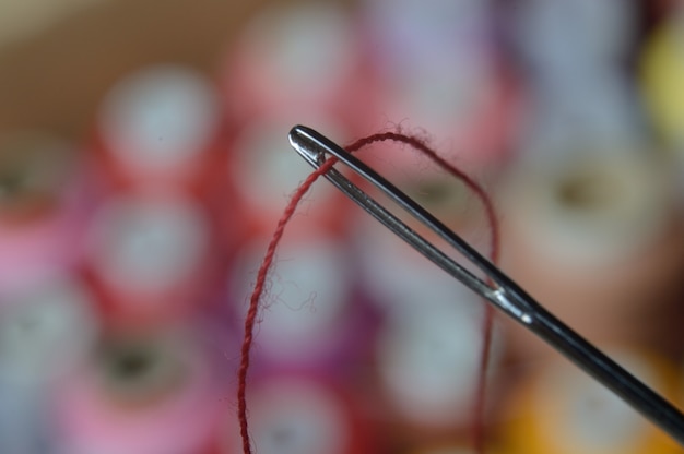 Uma agulha de costura com linha vermelha passando pelo buraco da agulha