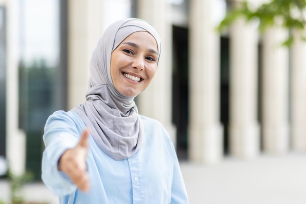 Uma alegre mulher muçulmana usando um hijab estende um aperto de mão simbolizando bem-vindo e acordo com um