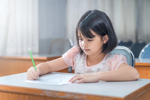 Uma aluna asiática se concentra escrevendo no papel do exame na classe