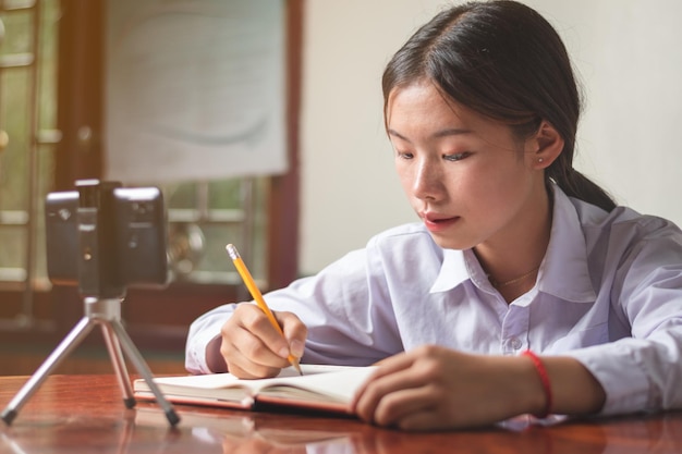 Uma aluna com traje de estudante está estudando on-line a partir do celular em casa com o professor de notas explicando o conhecimento sobre sua educação de livros e espaço de cópia de conceito de aprendizado on-line para texto