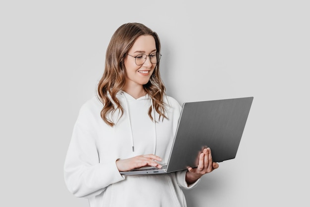 Uma aluna vestindo um moletom branco e óculos olha para a tela do laptop