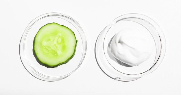 Uma amostra de um produto cosmético branco e um pedaço de pepino fresco em um fundo branco