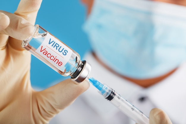 Uma ampola com a inscrição Virus Vaccine e uma seringa nas mãos de um médico cientista