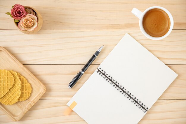 Uma área de trabalho com caderno, uma xícara de café e alguns biscoitos