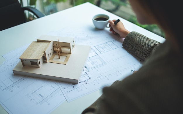 Uma arquiteta trabalhando em um modelo de casa de arquitetura com papel de desenho no escritório