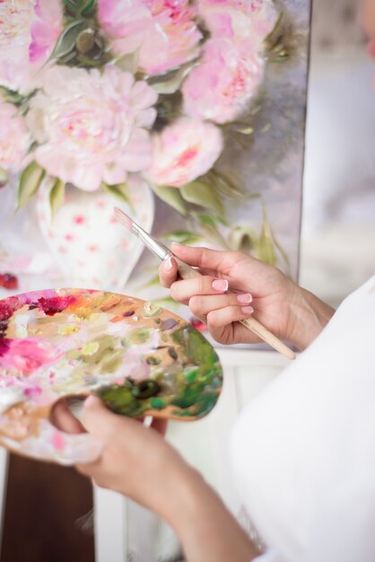 Uma artista de mulher mantém uma foto em um cavalete em casa. O pintor pinta pinturas a óleo.