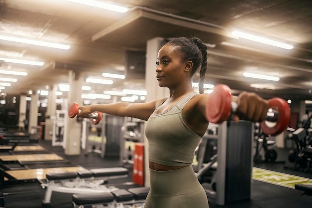 Uma atleta negra em forma está a treinar os ombros com halteres no ginásio.