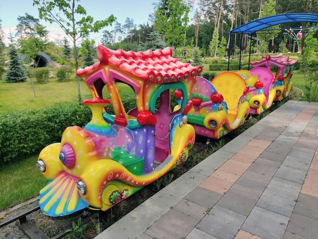 Uma atração de locomotiva infantil brilhante com vagões em um parque de diversões