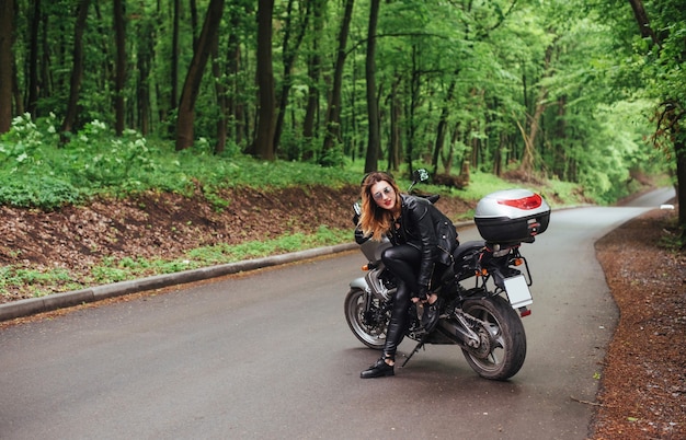Uma atraente garota sexy vestida de couro posando perto de uma moto esportiva do lado de fora