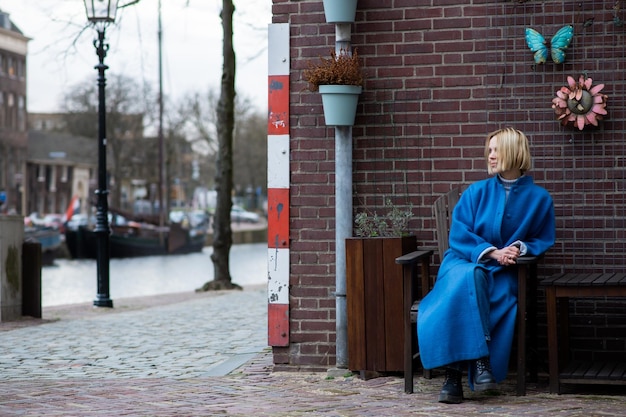 Uma atraente mulher adulta com um casaco azul olha para o lado Atrás dela está uma parede de tijolos Clima frio Viagens e aventuras