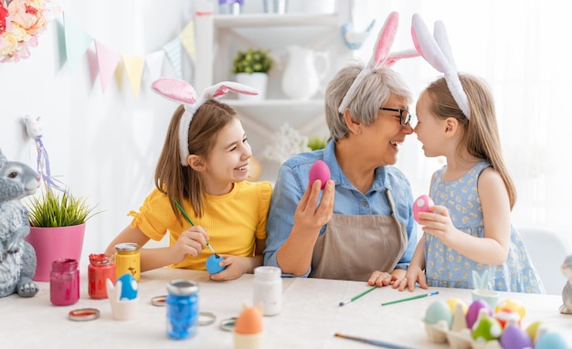 Uma avó e suas netas pintando ovos família feliz se preparando para a páscoa