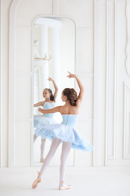 Uma bailarina bonita em traje de balé e na ponta dança perto do espelho. garota na aula de dança. a menina está estudando balé. bailarina está dançando. a dançarina está treinando no espelho.