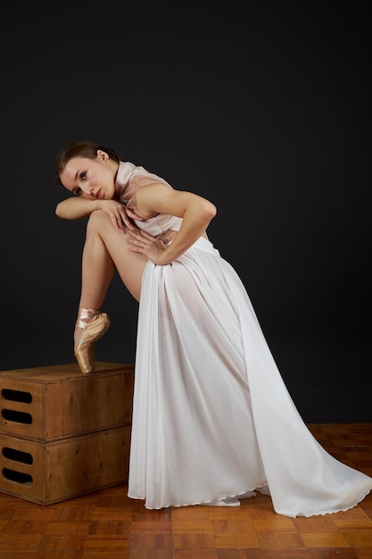 Foto uma bailarina em um vestido branco e sapatos de ponta fica em seus dedos dos pés e dança em um fundo preto