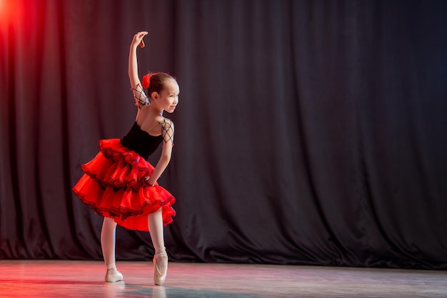 Uma bailarina menina está dançando no palco em um tutu em sapatilhas com castanholas a variação clássica de kitri