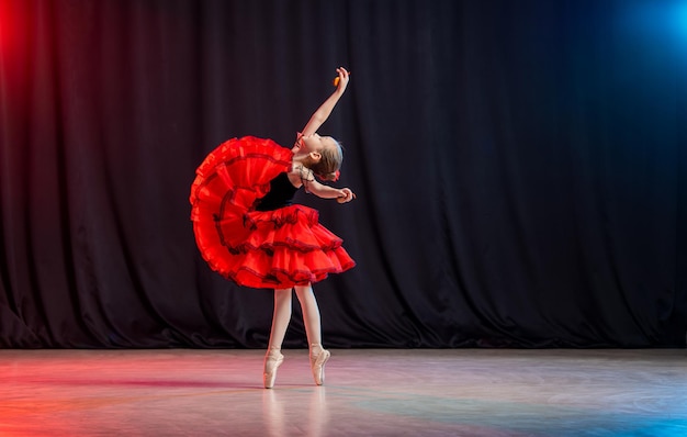 Uma bailarina menina está dançando no palco em um tutu em sapatilhas com castanholas a variação clássica de Kitri