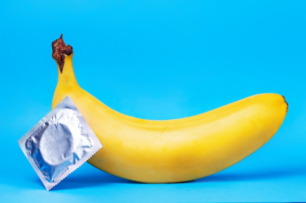 Uma banana amarela e um pacote de preservativo deitado ao lado no azul