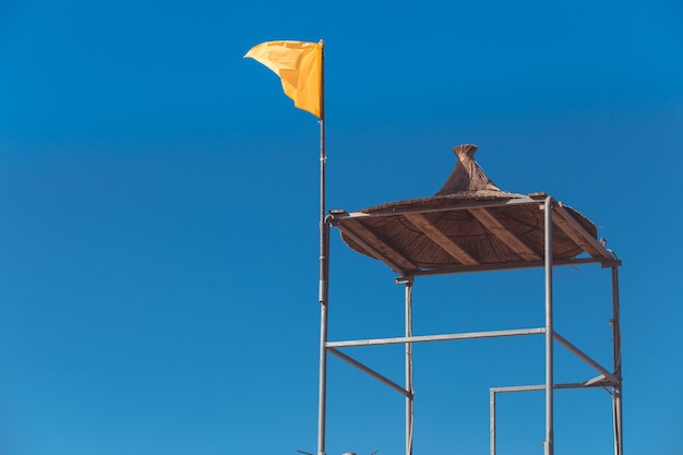Uma bandeira amarela voa de uma torre alta de salva-vidas no mar.