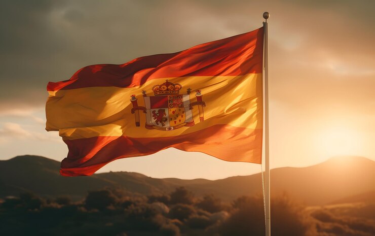 Foto uma bandeira espanhola com o sol se pondo atrás dela.