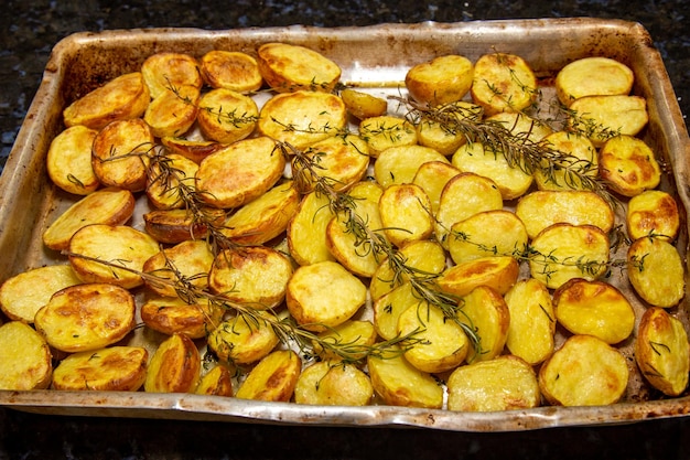 Uma bandeja de batatas assadas no forno com alecrim por cima.