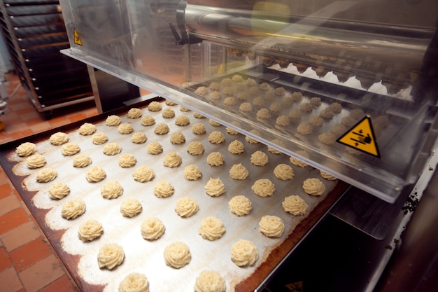 Foto uma bandeja de biscoitos prontos é retirada da esteira rolante na padaria
