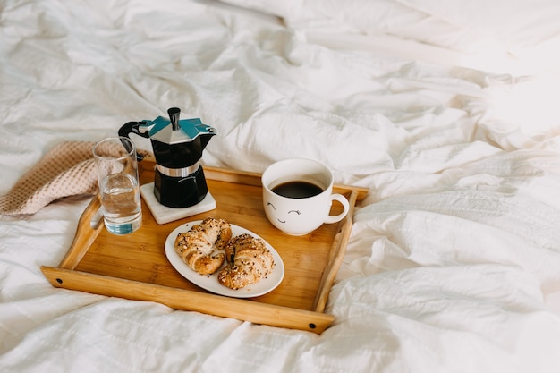 Uma bandeja de madeira com croissants e xícara de café na cama