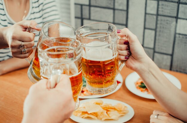 Uma bela cerveja em uma caneca segurando amigos e copos tilintar na mesa de cerveja