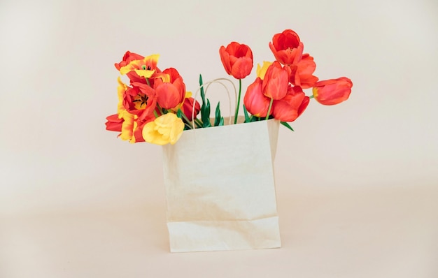 Uma bela composição de flores da primavera um buquê de tulipas vermelhas em um saco de papel em um fundo bege dia dos namorados feliz dia da mulher dia das mãesespaço para copiar