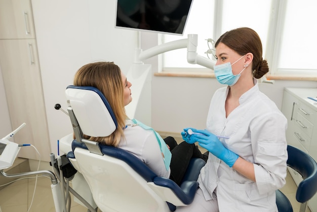 Uma bela dentista feminina está conversando com um paciente enquanto está sentado em uma cadeira explicação do conselho de consulta recomendação de um dentista