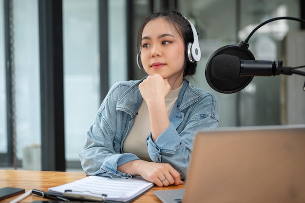 Uma bela e atenciosa apresentadora de rádio asiática senta-se em sua mesa em seu estúdio