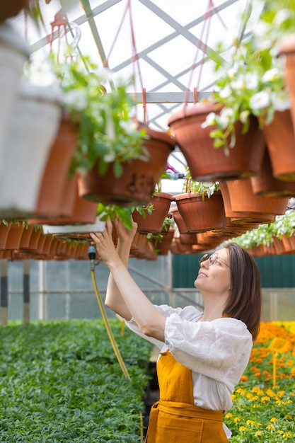 Uma bela e jovem jardineira adulta caucasiana em uma estufa ou viveiro de plantas cuida de