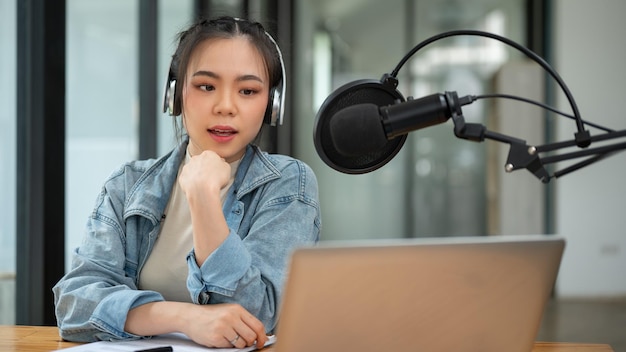 Uma bela e profissional apresentadora de rádio asiática fala em um microfone anunciando ou compartilhando notícias interessantes com seu público on-line durante seu programa on-air Jornalista DJ podcaster
