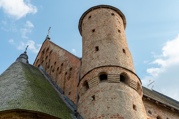 Uma bela e velha igreja fortaleza feita de tijolo vermelho contra um fundo de céu azul Uma torre defensiva com brechas de um castelo medieval