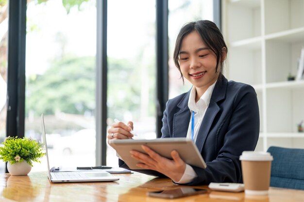 Uma bela empresária asiática ou contabilista está usando seu tablet em sua mesa no escritório