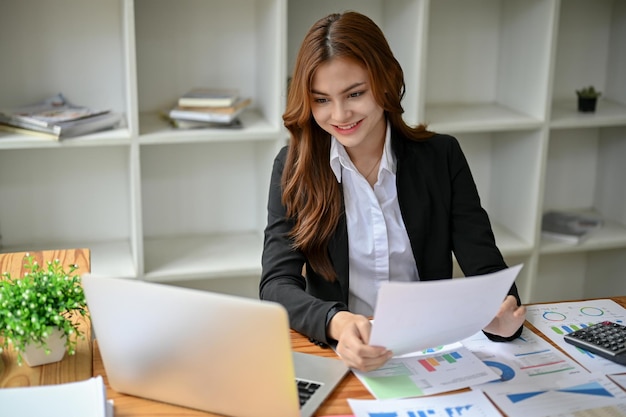 Uma bela empresária asiática usando seu laptop e trabalhando em relatórios de marketing em sua mesa