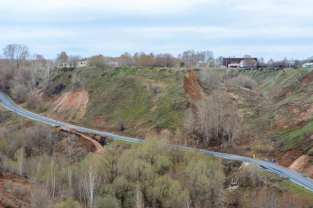 Uma bela estrada de montanha sobe. Uma estrada sinuosa que se estende até a distância, tendo como pano de fundo uma bela paisagem de primavera, floresta, montanhas, colinas e prados. O início da primavera.