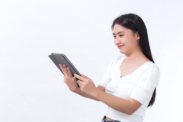 Uma bela estudante asiática em uma camisa branca olha feliz para o tablet em sua mão