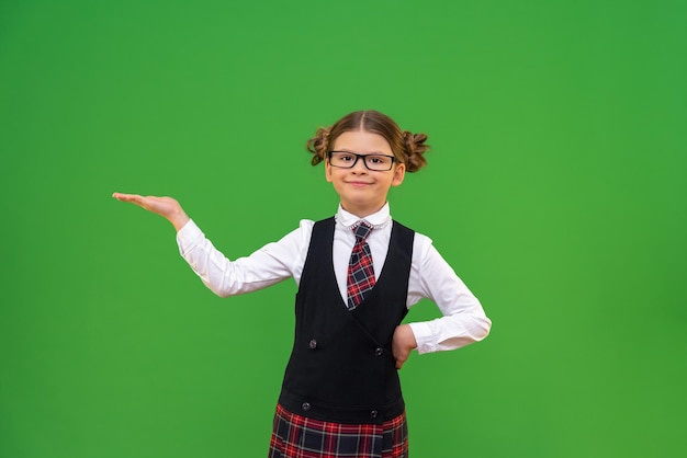 Uma bela estudante de óculos e uniforme escolar estendeu a mão e está segurando seu anúncio ou anúncio na mão.