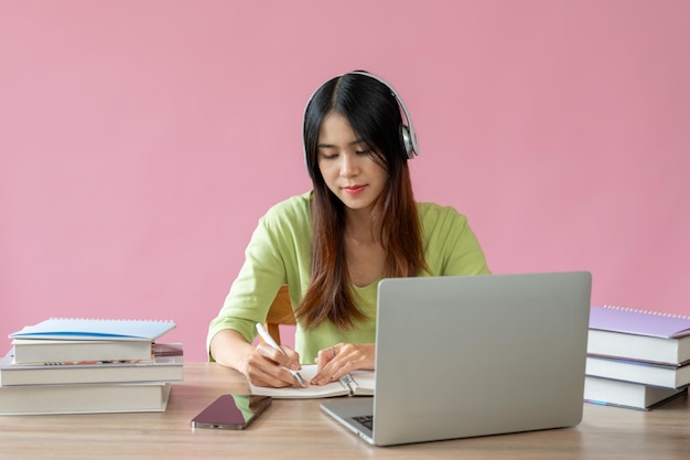 Uma bela estudante universitária asiática se concentra em estudar para uma aula online em sua mesa de estudo